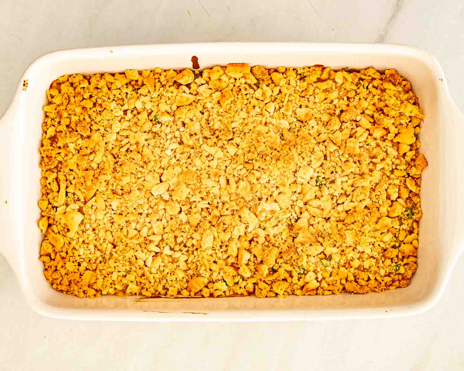 Overhead view of baked tuna noodle casserole in a white dish, covered with golden cracker crumbs and fresh parsley.