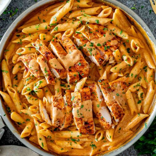 Overhead skillet of creamy garlic Parmesan chicken pasta topped with sliced seasoned chicken and scattered chopped parsley.