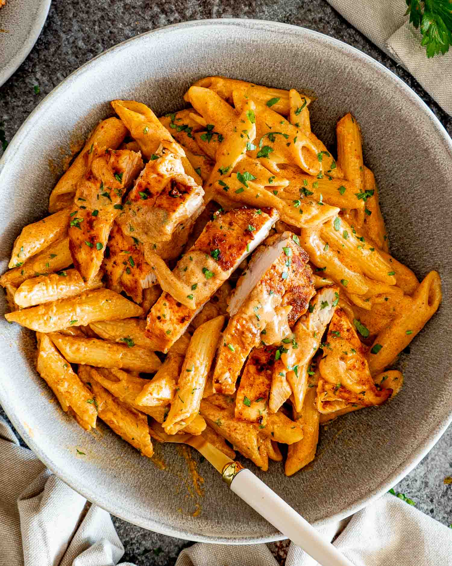 Overhead bowl of creamy garlic Parmesan chicken pasta with sliced chicken, golden sauce, penne, and fresh parsley.