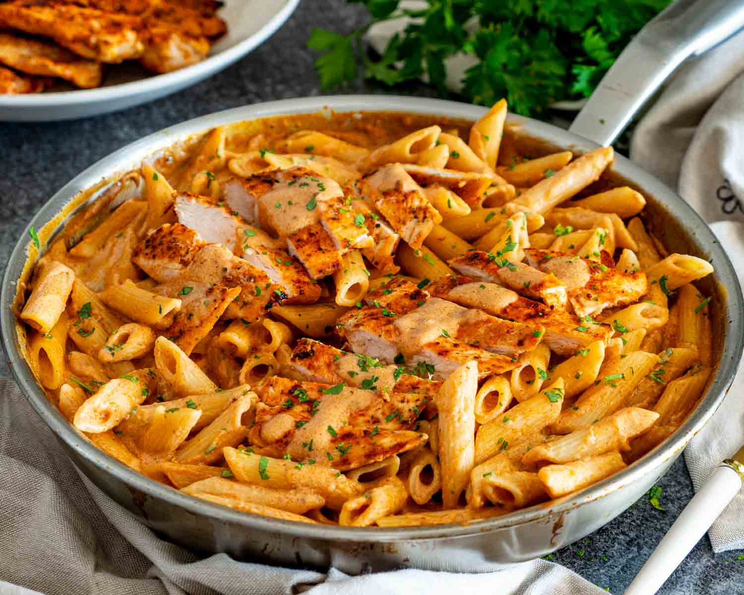 Skillet filled with creamy garlic Parmesan chicken pasta, featuring golden chicken slices, saucy penne, and chopped parsley.