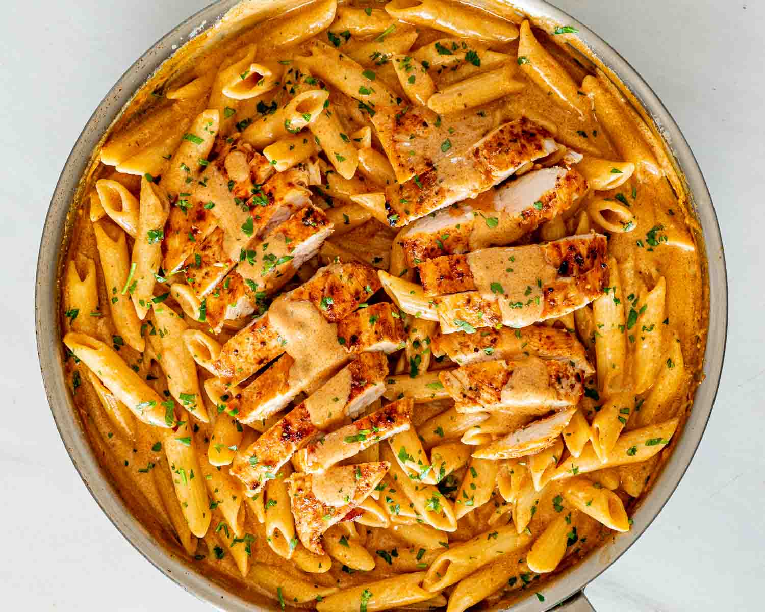 Overhead view of creamy garlic Parmesan chicken pasta with sliced chicken, penne, rich sauce, and chopped parsley.