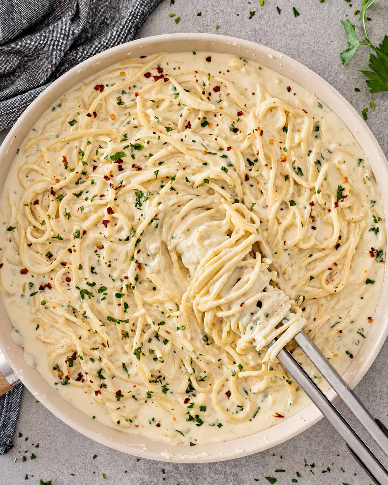 Overhead view of creamy Parmesan spaghetti in a skillet, garnished with parsley, red pepper flakes, and freshly grated cheese.
