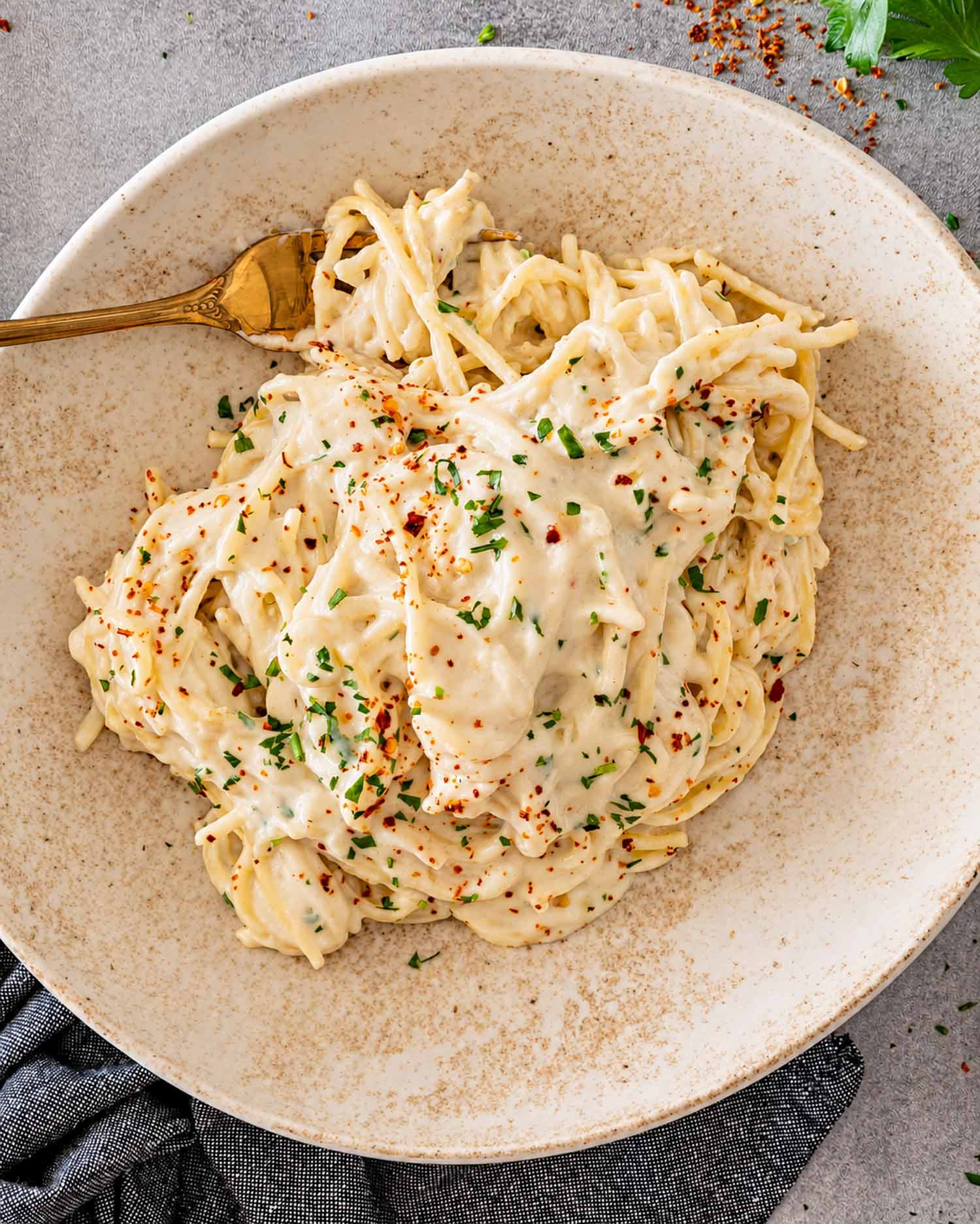 Creamy Parmesan spaghetti served in a rustic bowl with parsley, red pepper flakes, grated cheese, and a gold fork.