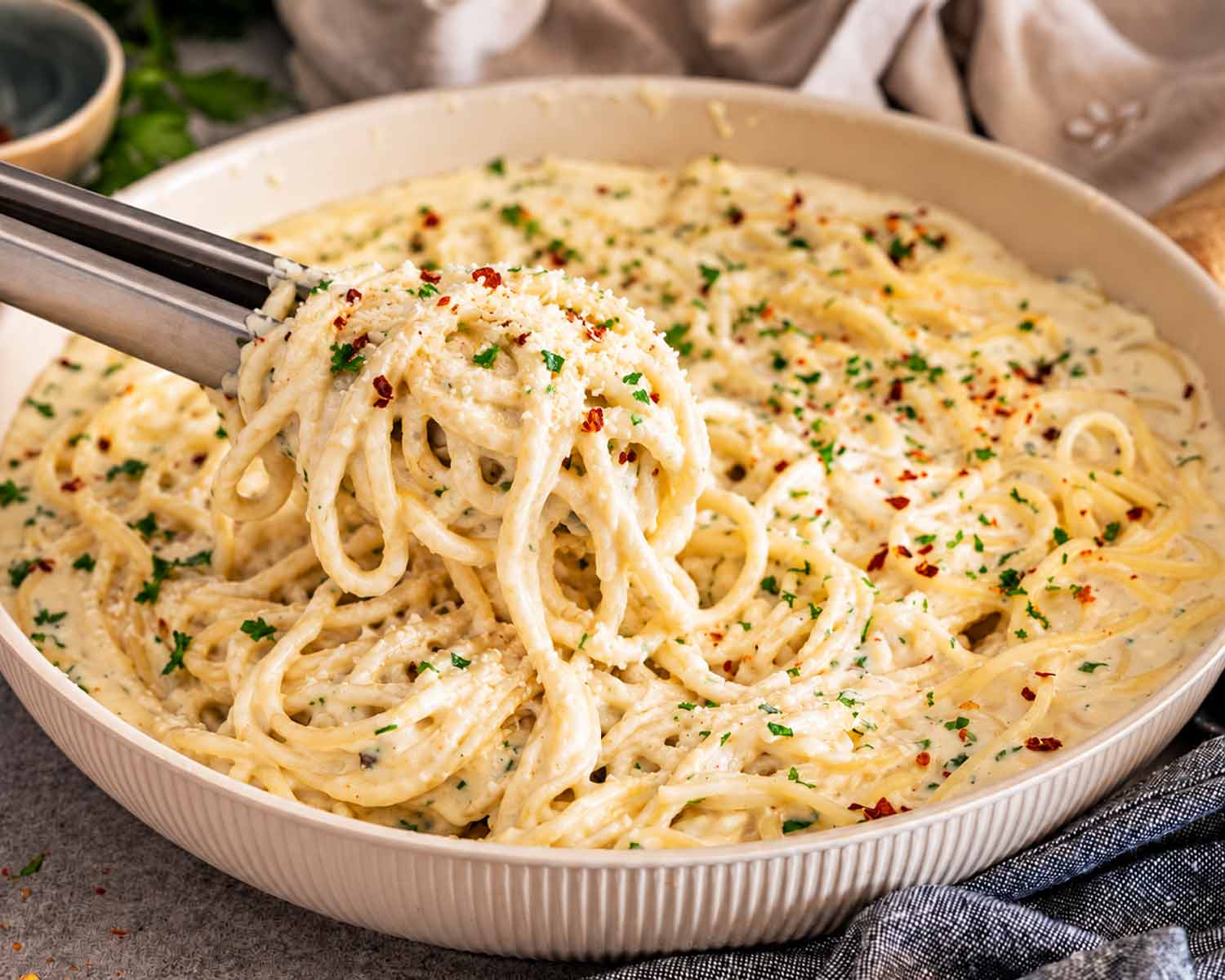A generous forkful of creamy Parmesan spaghetti is lifted above the skillet, showing the sauce-coated strands and fresh garnishes.