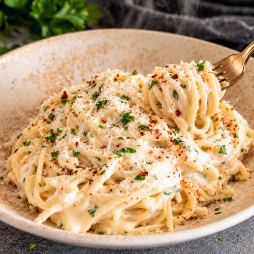 Creamy Parmesan spaghetti is twirled around a gold fork above a rustic bowl garnished with parsley and red pepper flakes.