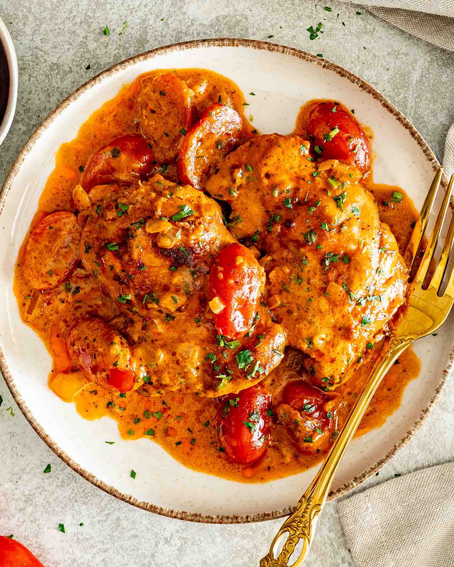 Overhead plate of creamy sun-dried tomato chicken thighs with cherry tomatoes, parsley, and a gold fork.