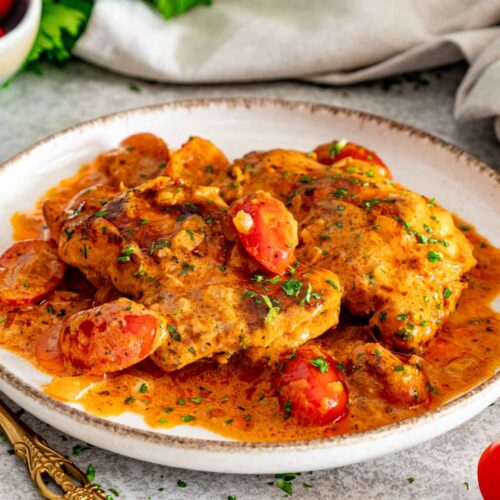 Plated creamy sun-dried tomato chicken thighs with cherry tomatoes, fresh parsley, and a rich orange cream sauce.