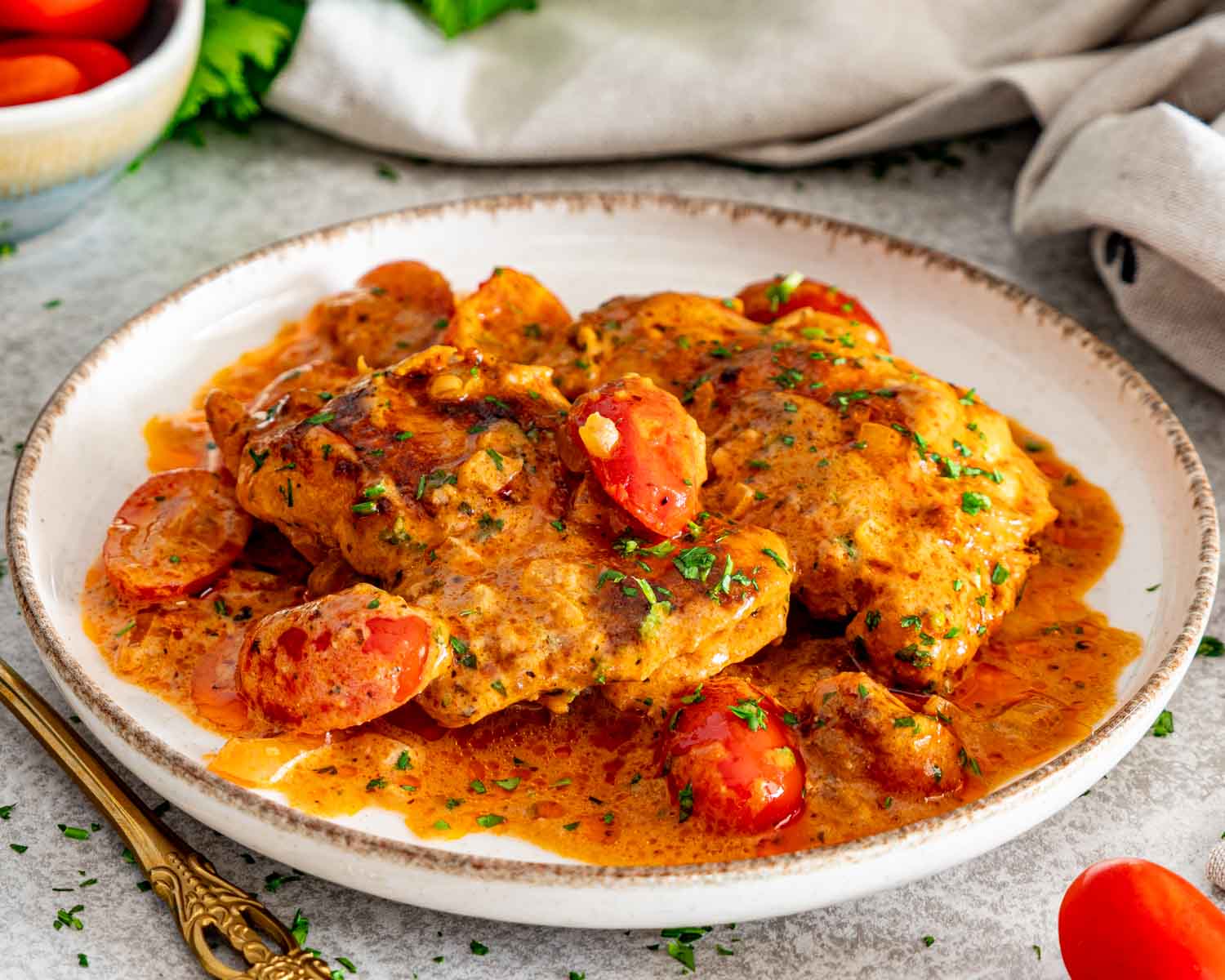 Plated creamy sun-dried tomato chicken thighs with cherry tomatoes, fresh parsley, and a rich orange cream sauce.