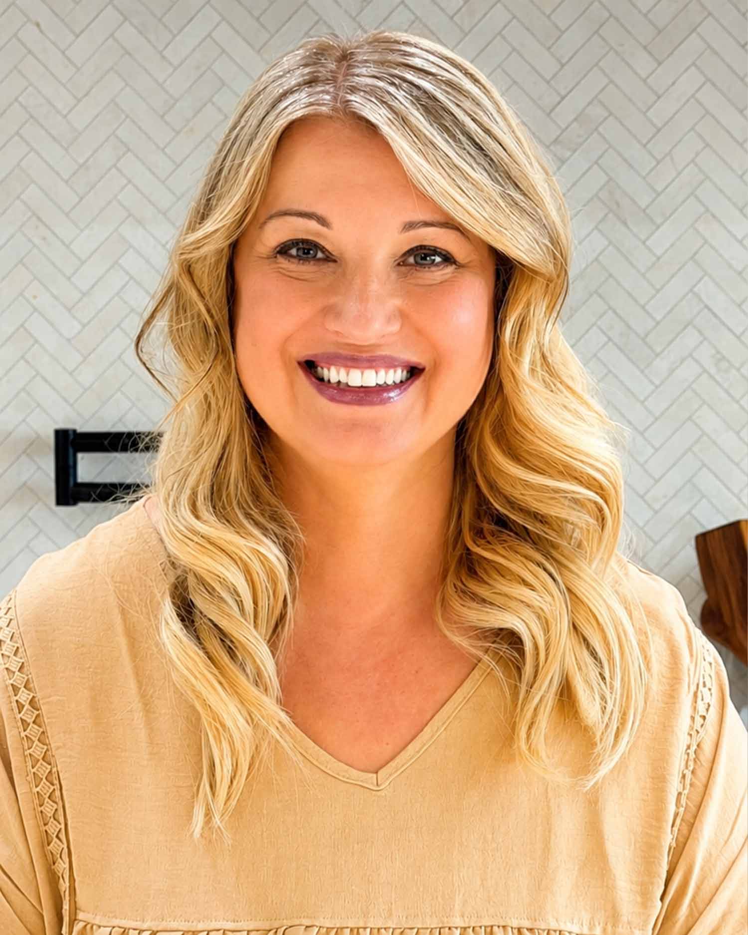 Joanna Cismaru smiling in her kitchen with long blonde wavy hair, wearing a black blouse after losing 150 pounds.