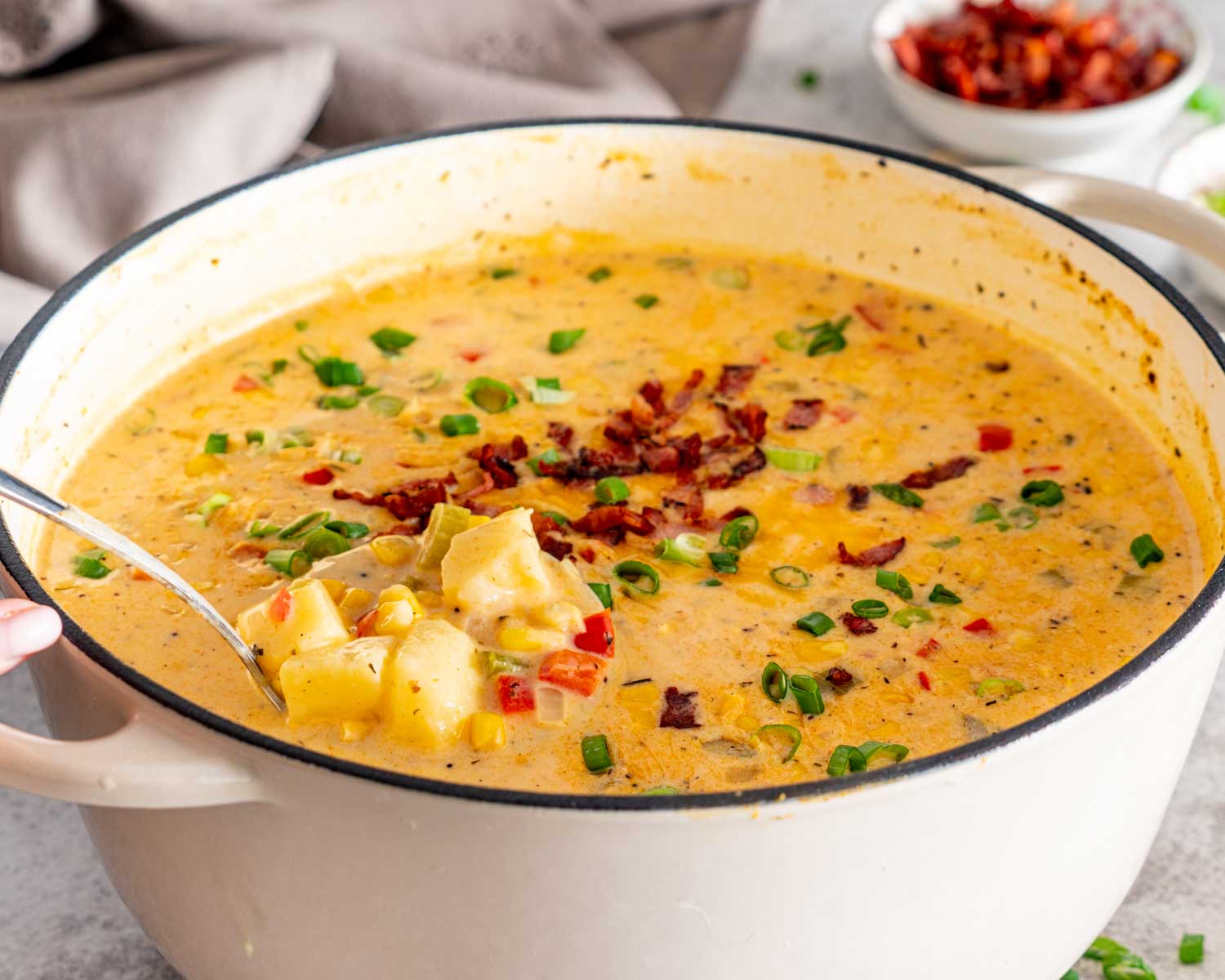 Loaded corn chowder in a Dutch oven with a spoonful of potatoes, corn, peppers, bacon, and creamy broth.