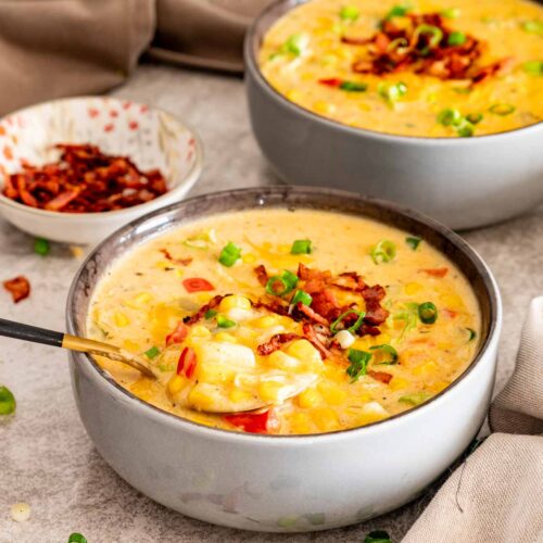 Spoon lifting a creamy bite of loaded corn chowder with potatoes, corn, bacon, cheddar, peppers, and green onions.