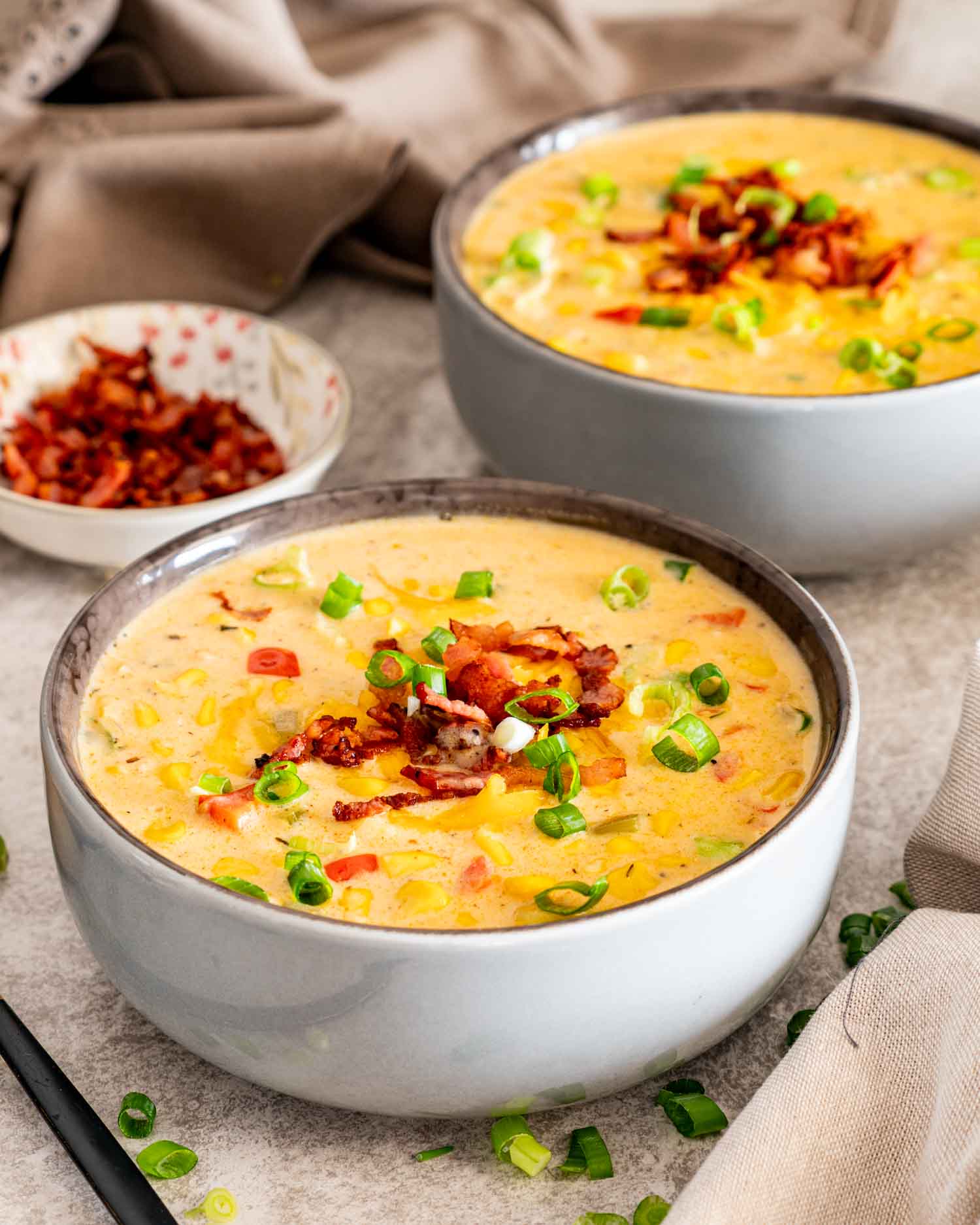 Two bowls of creamy loaded corn chowder garnished with crispy bacon, cheddar cheese, and sliced green onions.