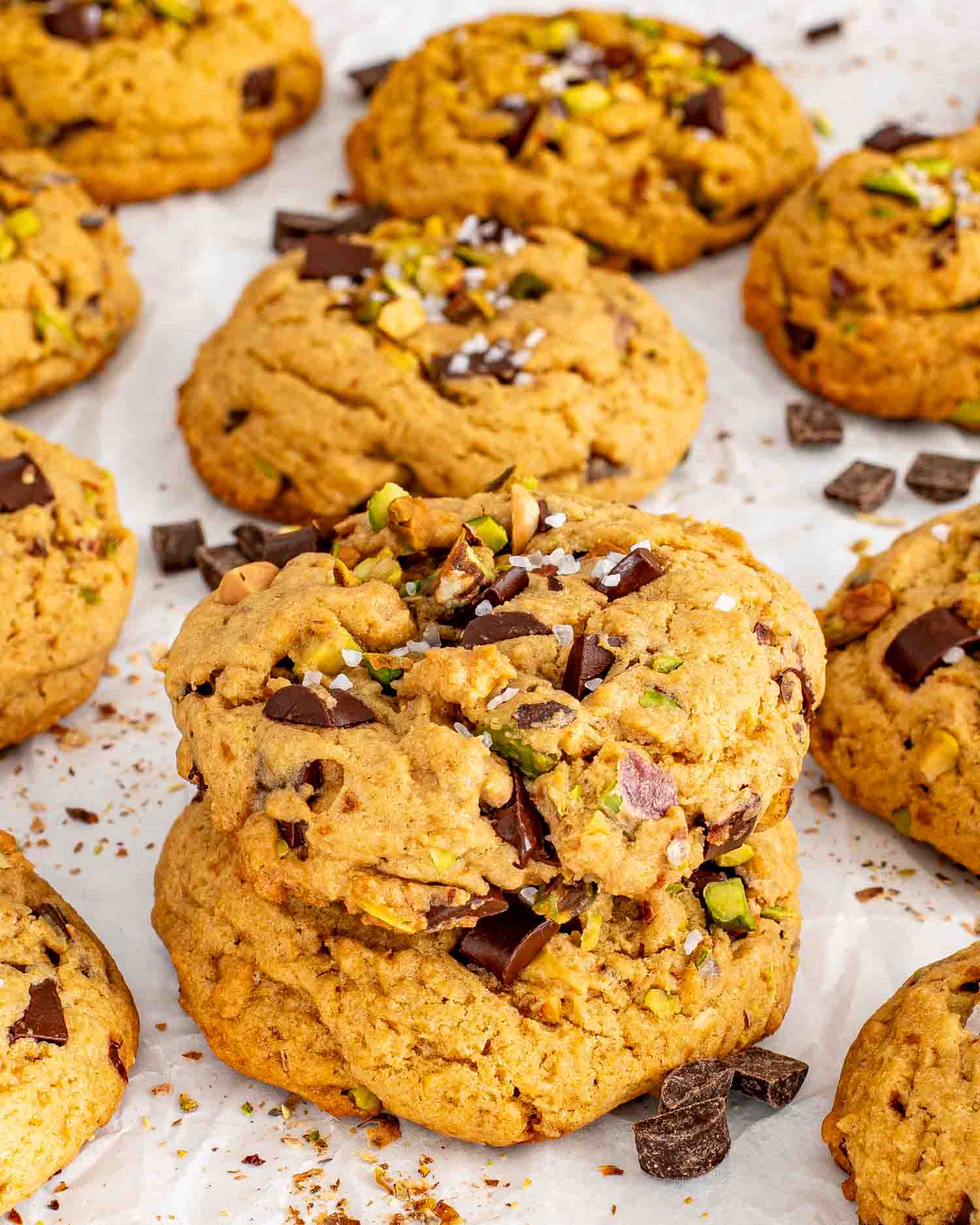 Broken pistachio chocolate chunk cookies reveal gooey melted chocolate among whole cookies scattered with pistachios and chocolate pieces.
