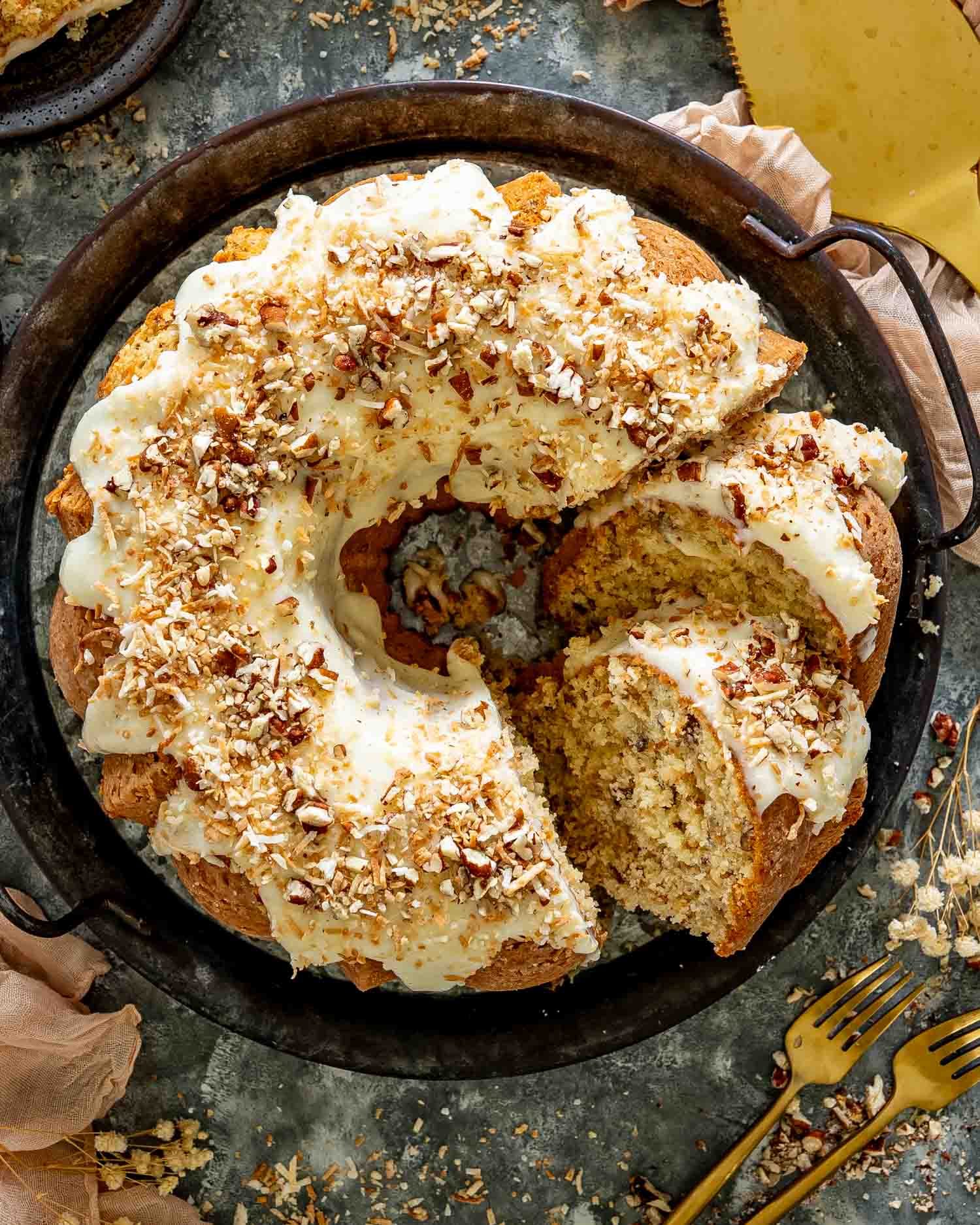 Overhead view of toasted coconut Italian cream Bundt cake with cream cheese glaze, chopped pecans, and one slice removed.