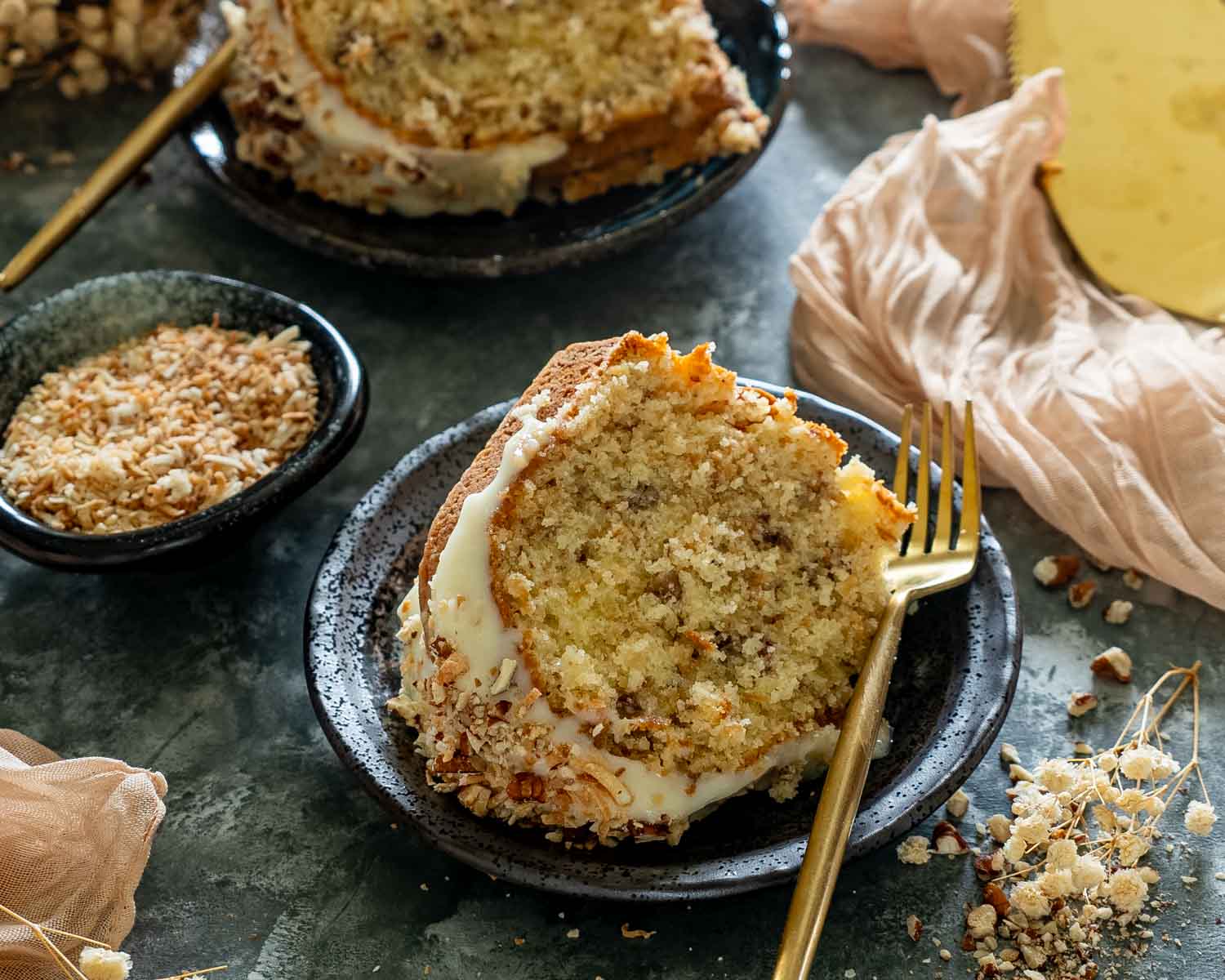 Moist slice of toasted coconut Italian cream Bundt cake served with cream cheese glaze, chopped pecans, and toasted coconut.