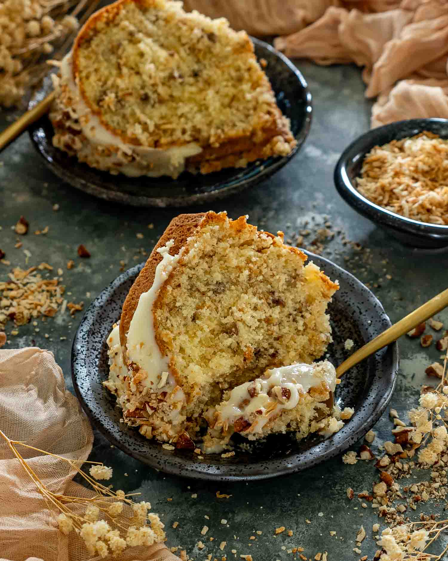 Partially eaten slice of toasted coconut Italian cream Bundt cake served on a black plate with creamy glaze.