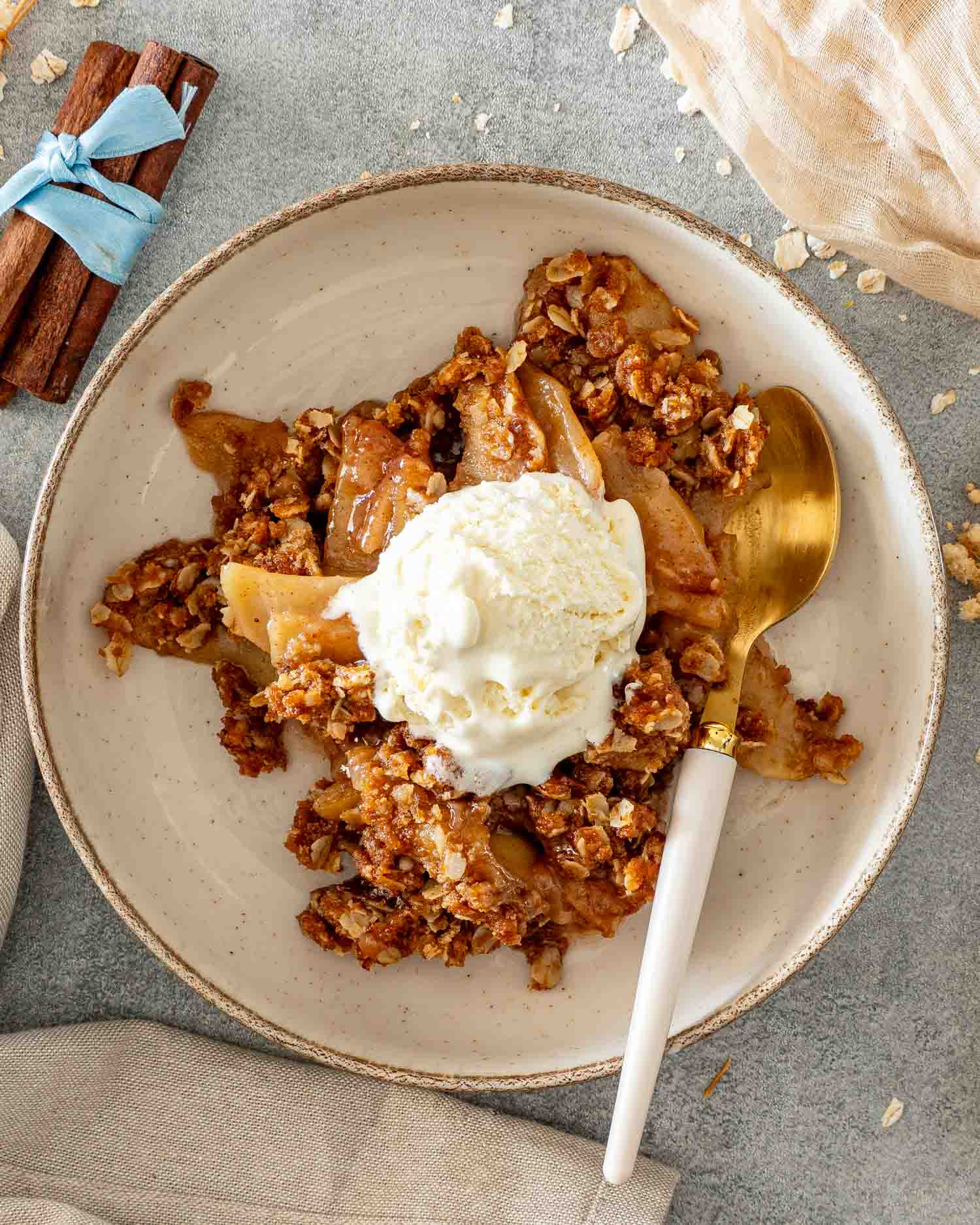 Overhead view of warm apple crisp and vanilla ice cream served in a bowl with a gold and white spoon.