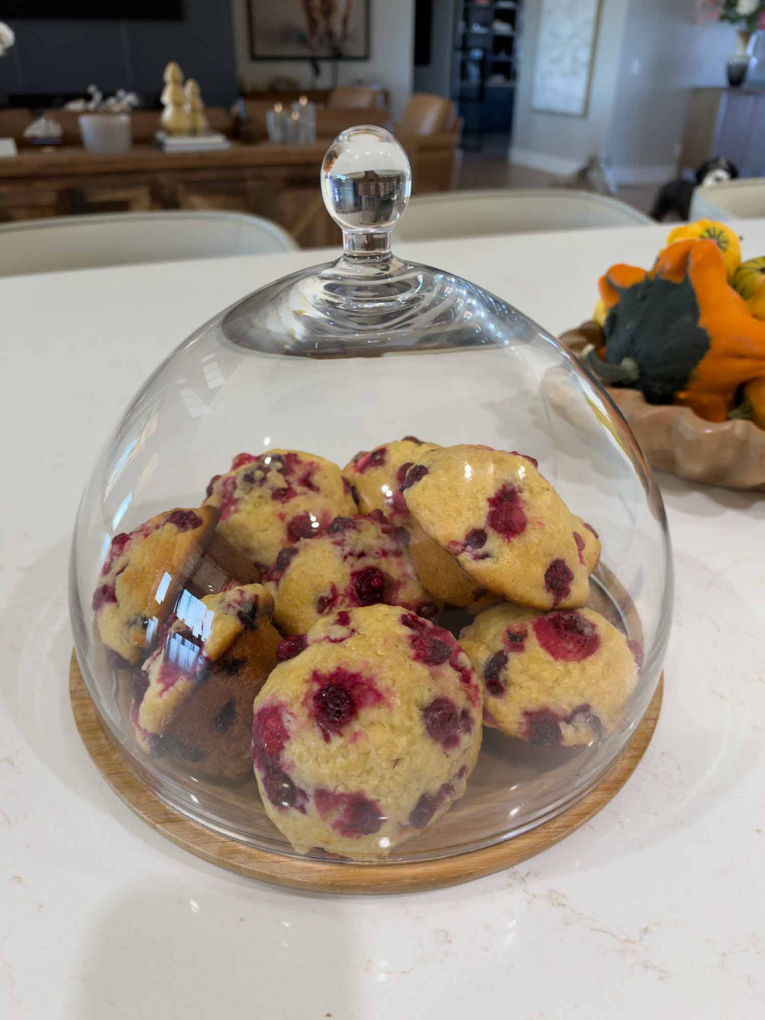 Freshly baked berry muffins displayed under a glass cake dome on a wooden stand in Joanna's farmhouse kitchen.
