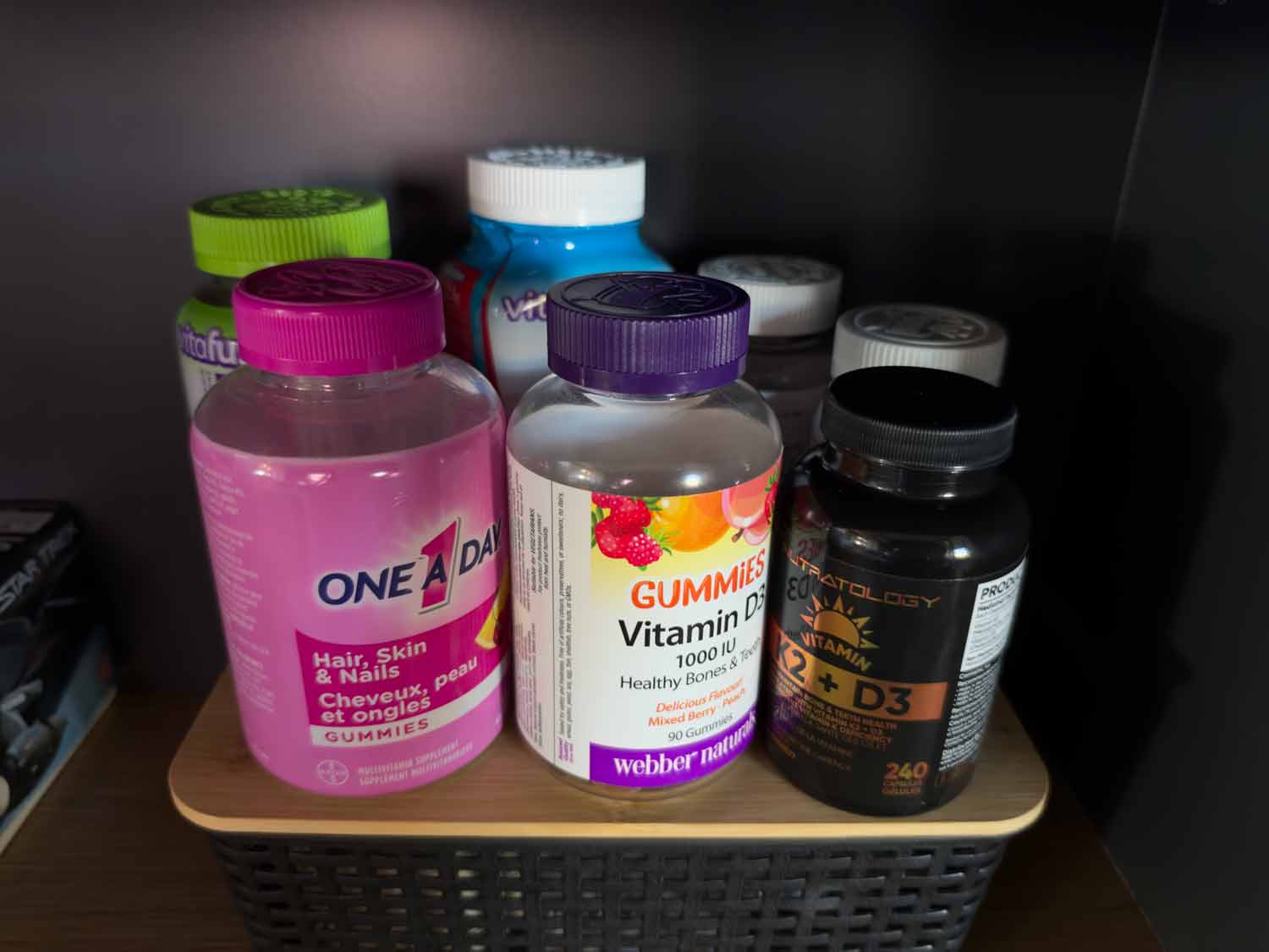 Assortment of daily vitamin supplements, including vitamin D3, K2, and hair, skin, and nail gummies, arranged on a shelf.