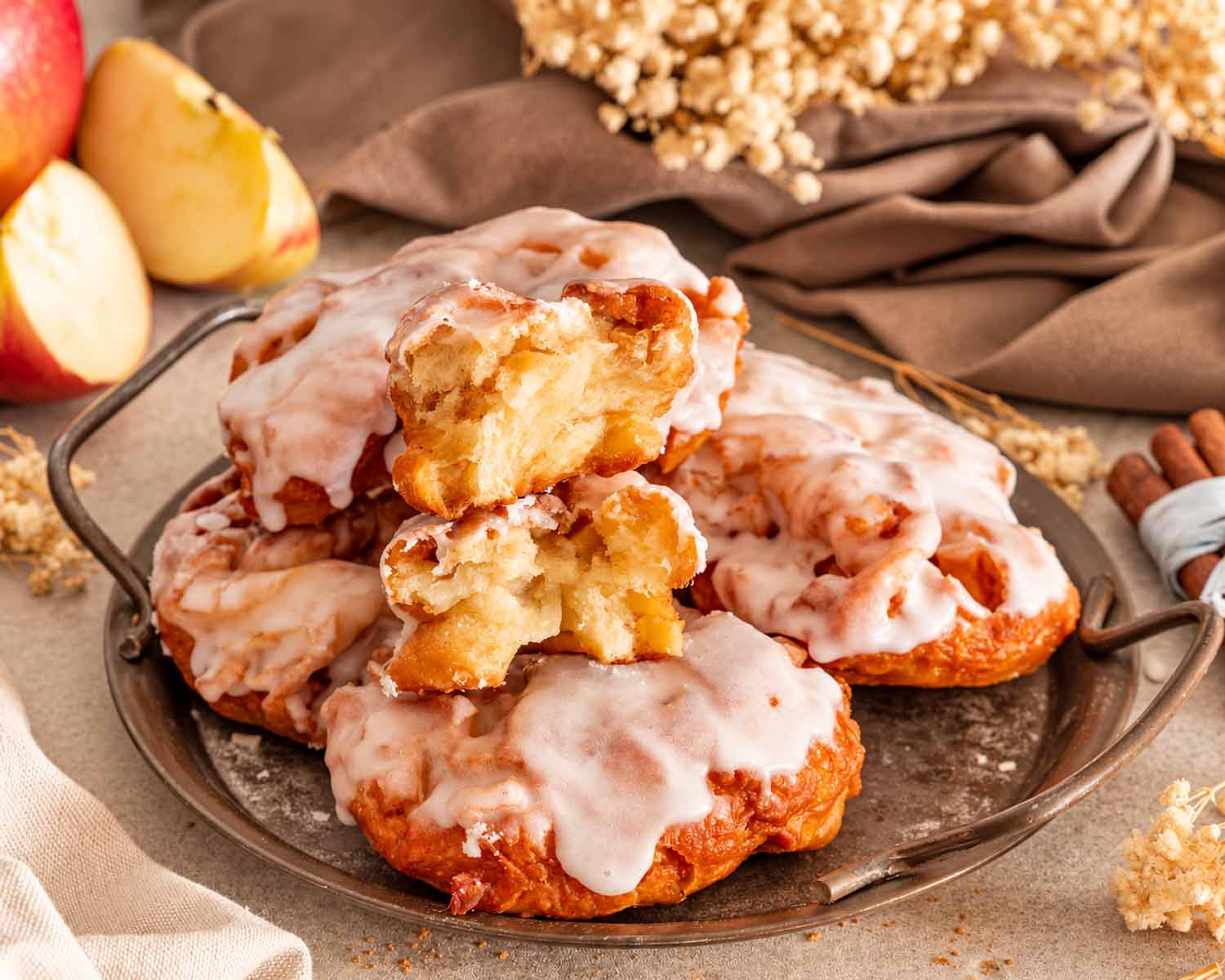 Glazed apple fritters with two broken-open pieces revealing a soft apple-filled interior on a rustic serving tray.