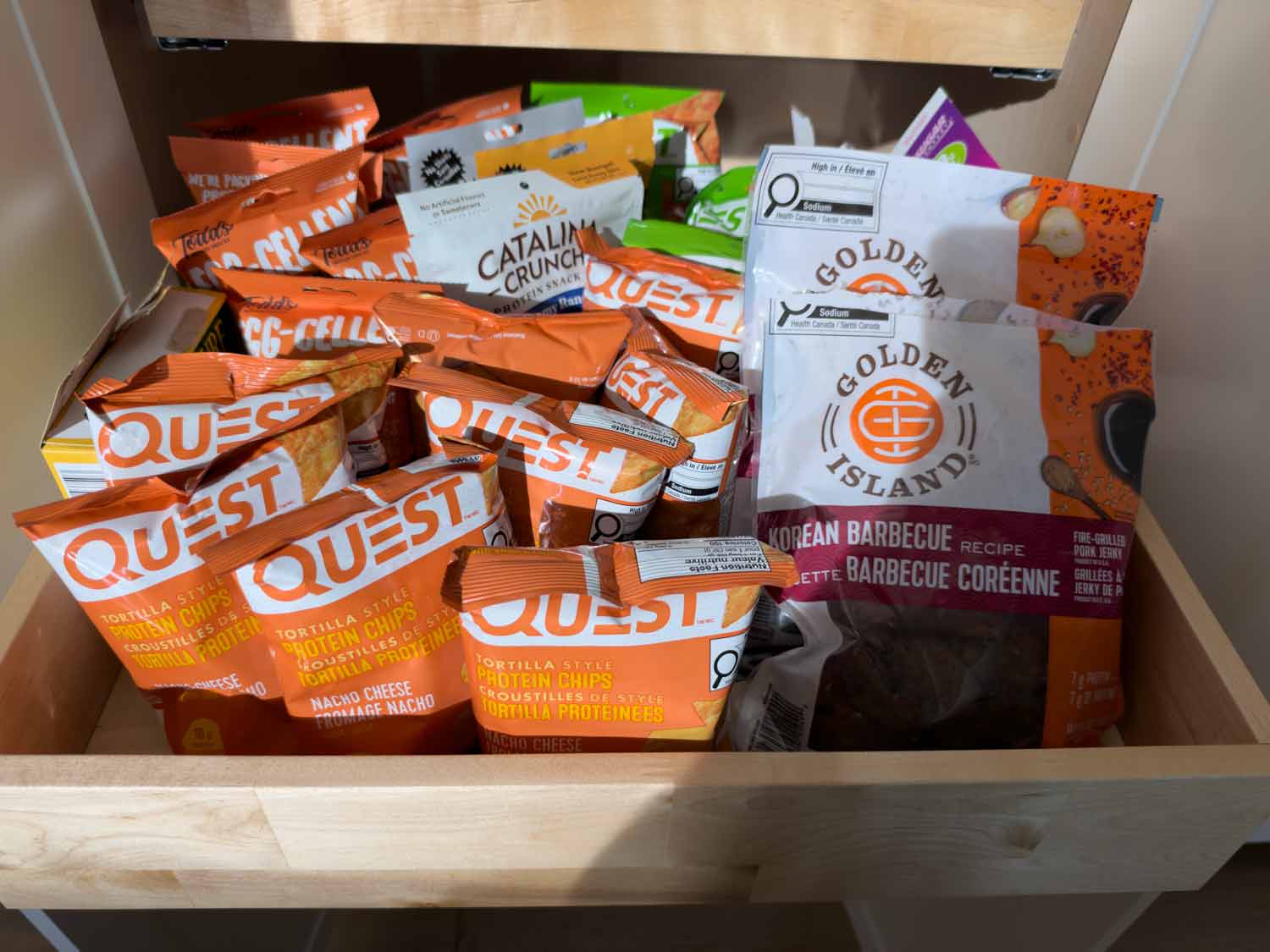 Open kitchen drawer stocked with Quest protein chips, Catalina Crunch snacks, and Golden Island jerky for convenient high-protein snacking.