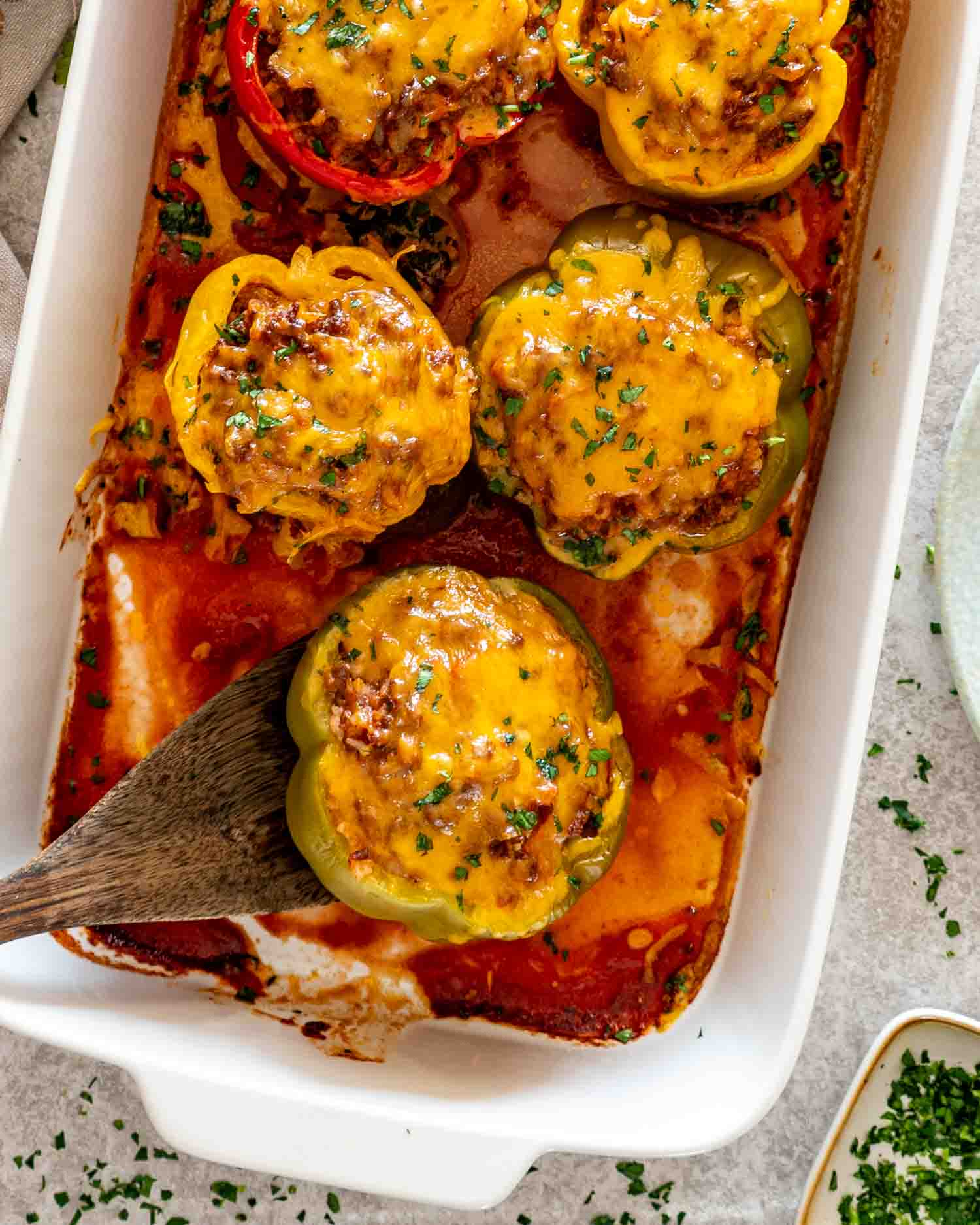 Overhead view of colorful stuffed peppers baked with melted cheddar, parsley, and tomato sauce in a casserole dish.