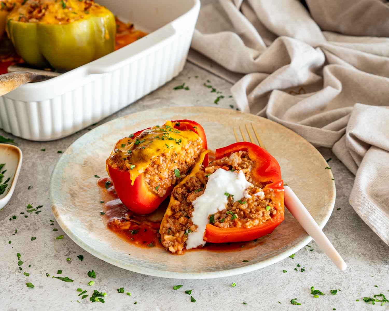 Sliced stuffed red pepper served on a plate with creamy topping, with more baked peppers in the background.